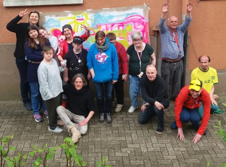 Gruppenfoto mit ca 14 Personen vor einem bunten Graffiti-Plakat