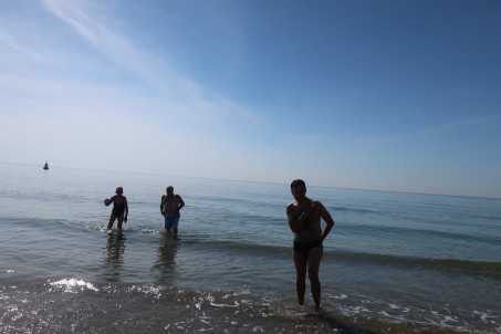 drei Personen stehen bis zu den Knien im Meer. Die Sonne scheint.