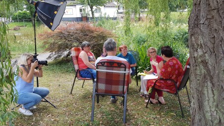 fünf Personen sitzen im Kreis unter einem Baum. Eine Frau macht Fotos.