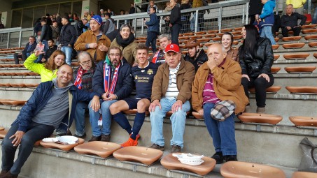 Eine Gruppe Menschen mit Behinderung sitzt auf der Tribüne des SC Bonn rund um Stürmer Marcel Kaiser.